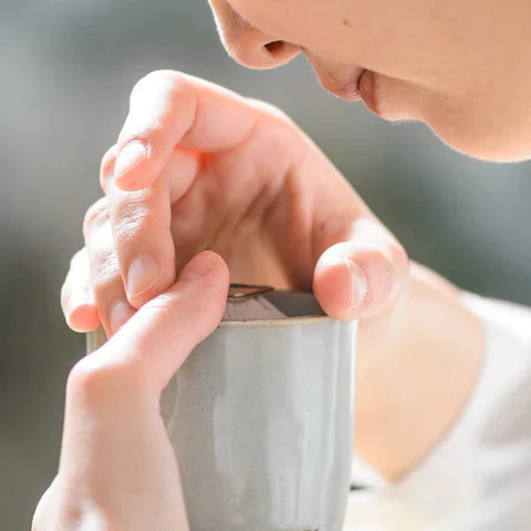 A person cupping a small white vessel near their face to appreciate its aroma.