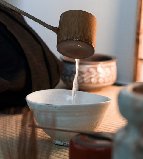 Hot water being ladled with a bamboo hishaku into a tea bowl during a Japanese tea ceremony, with steam rising.