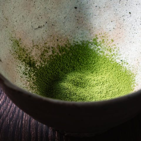 Close-up of vivid green matcha powder spread across a dark surface, showing its fine texture.