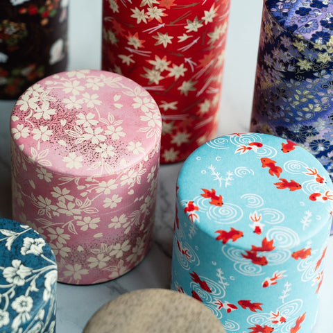 A group of decorative Japanese tea canisters covered in washi paper with cherry-blossom and goldfish patterns.