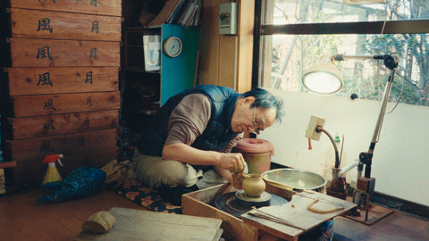 Wide view of the Fugetsu studio, the potter at his wheel below wooden plaques brushed with the kiln's name