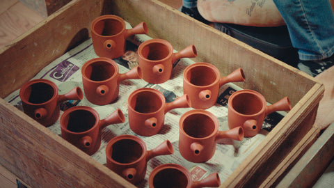 Wooden tray of unfired Gyokko kyusu in red clay, spouts and handles attached, drying in the workshop