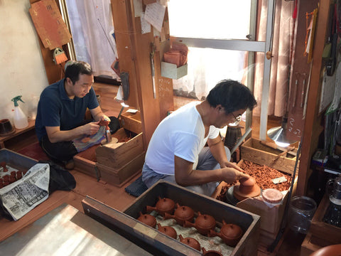 Father and son of the Gyokuryu workshop shaping kyusu side by side in their sunlit studio