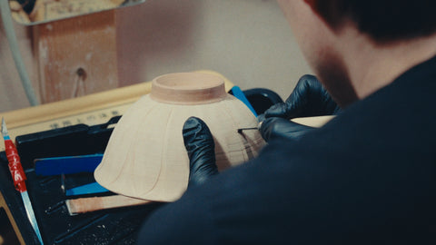 Gloved hands turning a bisque bowl upside down to trim its foot ring at the bench