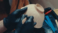 Gloved hands carving a fine line into the side of an unglazed bowl