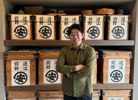 Man standing in front of shelves with wooden boxes featuring Japanese text