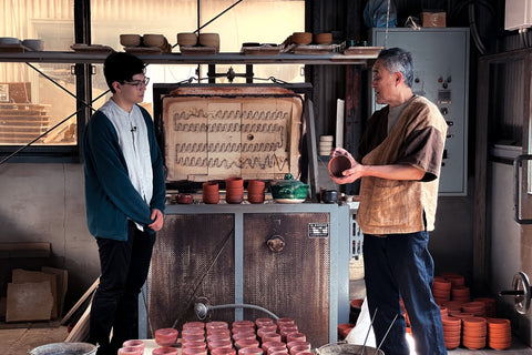 David and Sasaki Shōraku in a pottery studio with clay pots and a kiln.