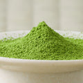 Bright green Betsugi matcha powder mounded in a ceramic bowl, side view.