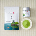 Tezumi Classics Eiryoku matcha pouch with a stone lantern and koi pond design beside a silver tin and a dish of matcha powder.