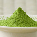 Deep green Eiryoku matcha powder heaped in a cone in a cream ceramic bowl, side view.