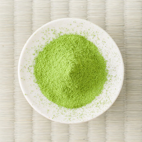 Green Eiryoku matcha powder mounded in a white dish on a tatami mat, overhead view.