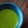 Whisked green usucha in a blue-glazed tea bowl on a wooden table, viewed from above.