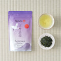 Purple Fujimien Sencha pouch with a crane and red sun motif, shown on tatami with a cup of brewed tea and a dish of leaf