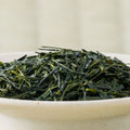 Close-up of Fujimien sencha leaf, slender deep green needles with bright green flecks, heaped in a pale bowl