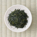 Fujimien sencha leaf on a small white dish, fine dark green needles flecked with pale stem, seen from above
