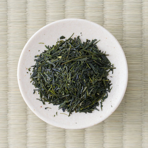 Fujimien sencha leaf on a small white dish, fine dark green needles flecked with pale stem, seen from above