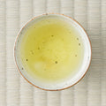 Fujimien sencha brewed to a soft golden-green liquor in a speckled white cup, photographed from above