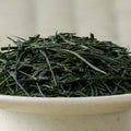 Dry deep-green handpicked Honyama Yabukita sencha leaves mounded in a ceramic bowl, side view.