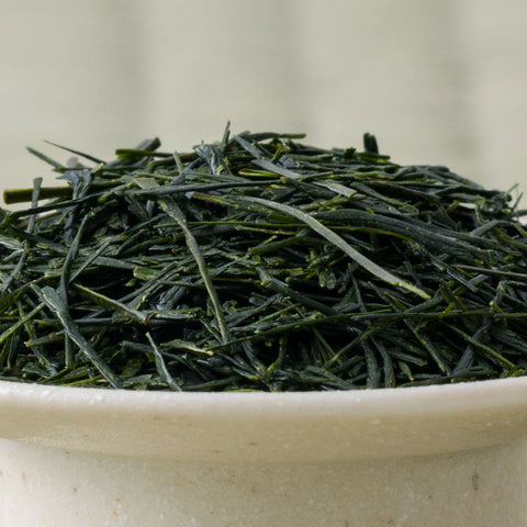 Dry deep-green handpicked Honyama Yabukita sencha leaves mounded in a ceramic bowl, side view.