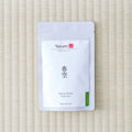 White Tezumi Specialty pouch printed 春空 / Haru-Sora Sencha with a green sencha tab, lying on a tatami mat