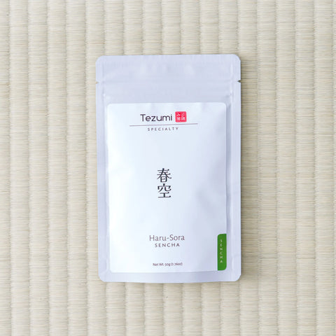 White Tezumi Specialty pouch printed 春空 / Haru-Sora Sencha with a green sencha tab, lying on a tatami mat
