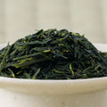 Close-up of deep green needle-shaped Haru-Sora sencha leaf heaped in a pale stoneware bowl