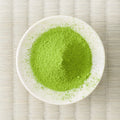 Vivid green Haruto matcha powder mounded in a white dish on a tatami mat, overhead view.