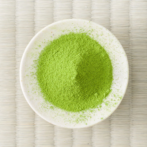 Vivid green Haruto matcha powder mounded in a white dish on a tatami mat, overhead view.