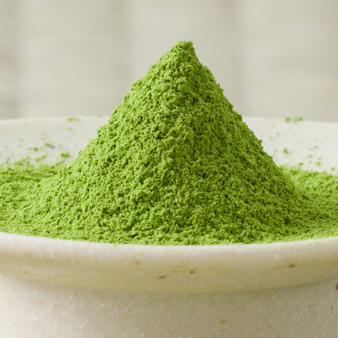 Bright green Hika matcha powder heaped in a tall cone in a cream ceramic bowl, side view.