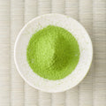 Bright green Hika matcha powder mounded in a white dish, viewed from above on a tatami mat.
