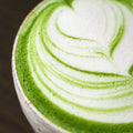 Close overhead view of a matcha latte with green-and-white leaf latte art in a ceramic cup.