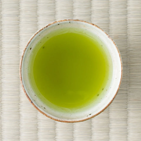 Hōjō Genmaimatcha brewed to a vivid yellow-green in a speckled white cup, photographed from above