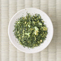 Overhead view of genmaimatcha on a small white dish, dark sencha leaf mixed with pale puffed rice