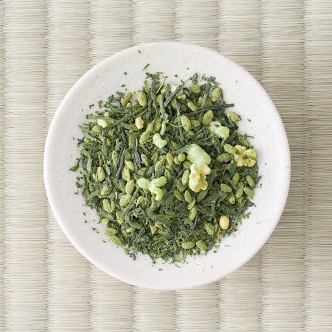 Overhead view of genmaimatcha on a small white dish, dark sencha leaf mixed with pale puffed rice