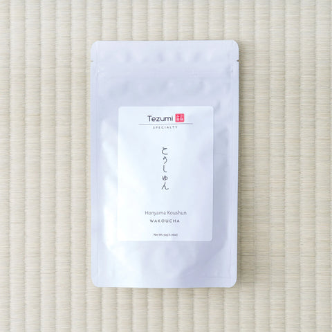 White Tezumi Specialty pouch labelled こうしゅん / Honyama Koushun Wakoucha, lying flat on a tatami mat