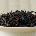 Close-up of dry Honyama Koushun wakoucha leaves, tightly curled and dark, heaped in a pale stoneware bowl