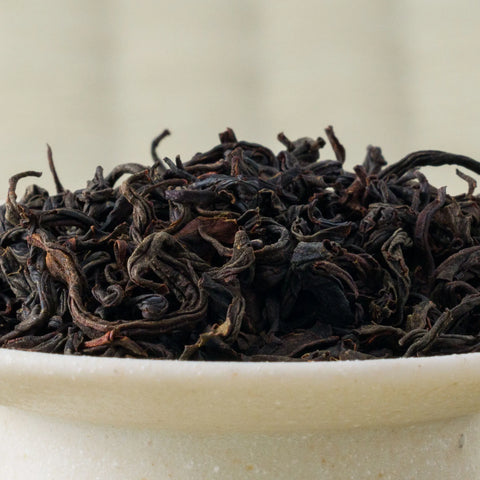 Close-up of dry Honyama Koushun wakoucha leaves, tightly curled and dark, heaped in a pale stoneware bowl