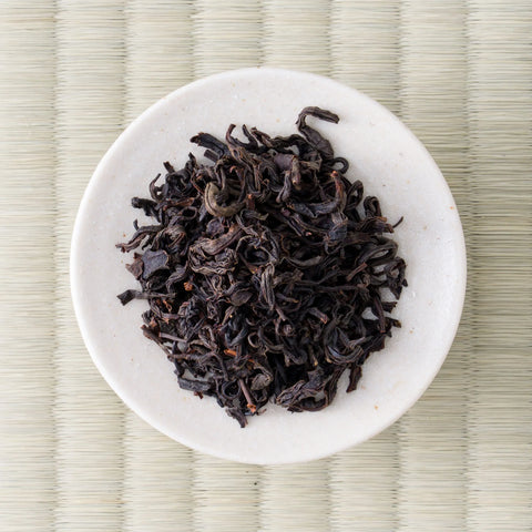Dark twisted leaves of Honyama Yabukita wakoucha arranged on a small white dish, viewed from directly above