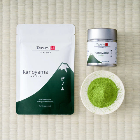 Tezumi Classics Kanoyama matcha pouch with a dark green mountain design beside a silver tin and a dish of matcha powder on a tatami mat.