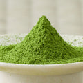 Bright green Kanoyama matcha powder heaped in a cone in a cream ceramic bowl, side view.