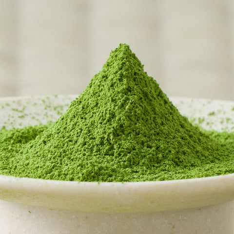 Bright green Kanoyama matcha powder heaped in a cone in a cream ceramic bowl, side view.
