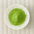 Green Kanoyama matcha powder mounded in a white dish on a tatami mat, overhead view.