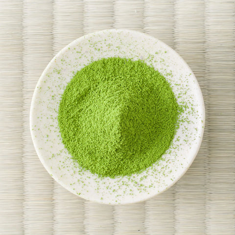 Green Kanoyama matcha powder mounded in a white dish on a tatami mat, overhead view.