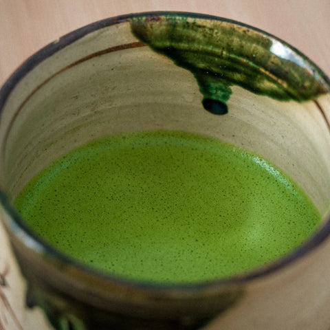 Whisked green matcha in an oribe-style tea bowl with a green glaze drip at the rim, viewed from above.