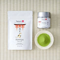 Tezumi Classics Komiya matcha pouch with a red torii gate and calico cat design, beside a silver tin and a dish of matcha powder.