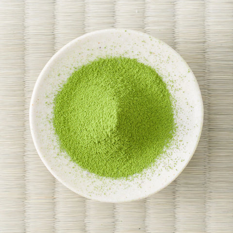 Green Komiya matcha powder mounded in a white dish, viewed from above on a tatami mat.