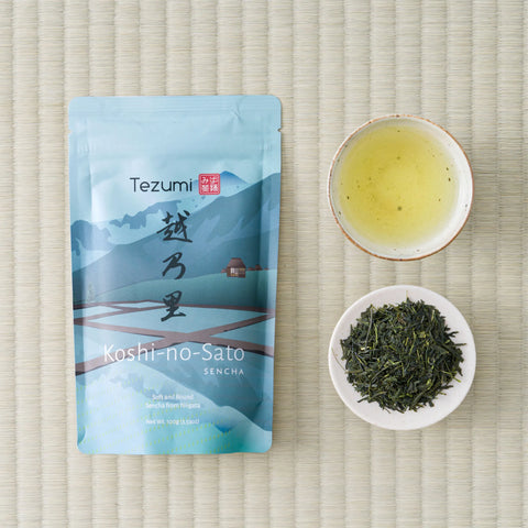 Pale blue Koshi-no-Sato Sencha pouch from Fujimien on tatami, beside a cup of brewed tea and a dish of dry leaf