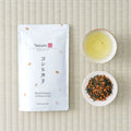 Tezumi Koshihikari Genmaicha pouch on tatami beside a cup of the brewed tea and a dish of the dry leaf