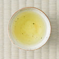 Brewed Koshihikari genmaicha, pale gold, in a speckled ceramic bowl set on a tatami mat