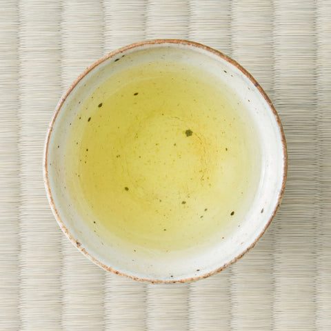 Brewed Koshihikari genmaicha, pale gold, in a speckled ceramic bowl set on a tatami mat